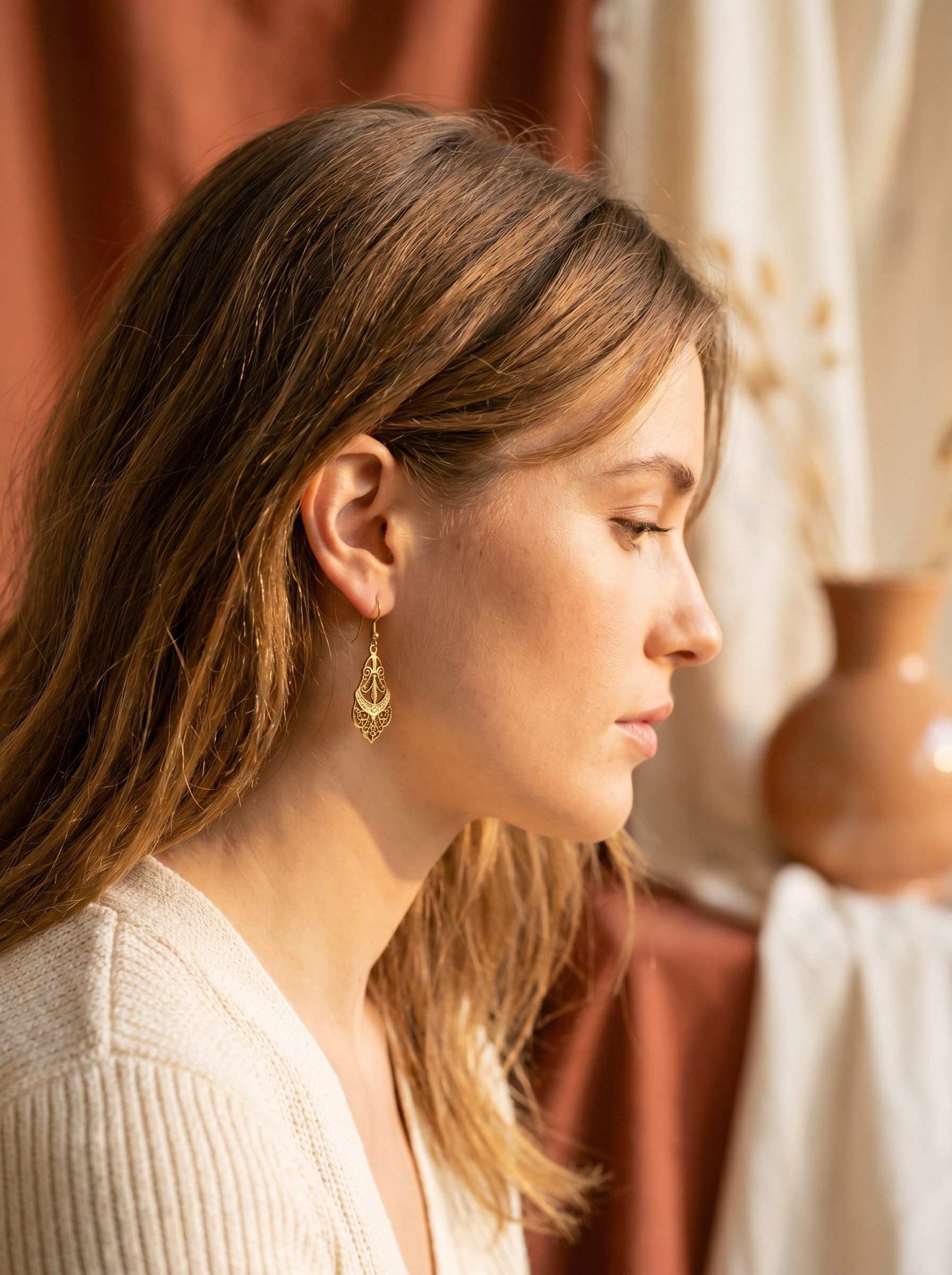 Gold drop earrings beside a soft profile in warm light
