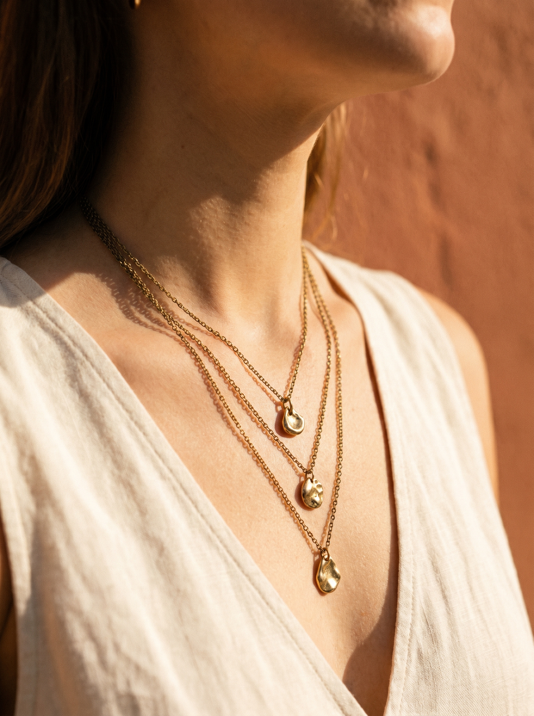 Layered gold pendant necklaces on warm ivory neckline